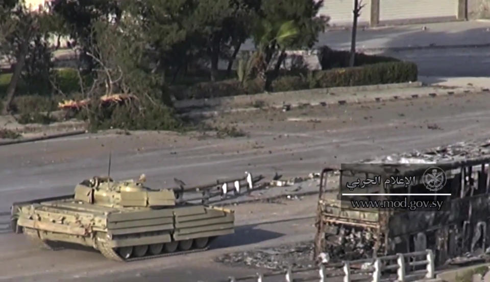 This frame grab from video provided by the government-controlled Syrian Central Military Media, shows a tank of Syrian troops passing by the remains of a burned bus, in an eastern neighborhood of Damascus, Syria, Wednesday, March. 22, 2017. Syrian troop are engaged in fighting with insurgents who have tried to breach government lines in eastern neighborhoods of the capital this week. The operation is spearheaded by the al-Qaida-linked Levant Liberation Committee. (Syrian Central Military Media, via AP)