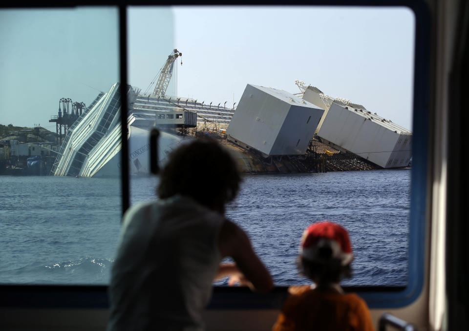 Passengers of a ferry look at the Costa Concordia cruise ship liying on its side in the Tuscan Island of Isola del Giglio, Monday, July 15, 2013. Salvage crews are working against time to right and remove the shipwrecked Costa Concordia cruise ship, which is steadily compressing down on itself from sheer weight onto its granite seabed perch off the Tuscan island of Giglio. Salvage master Nick Sloane said Monday that the Concordia has compressed some 3 meters (10 feet) since it came to rest on the rocks Jan. 13, 2012 after ramming a jagged reef during a stunt ordered by the captain that cost the lives of 32 people. (AP Photo/Gregorio Borgia)