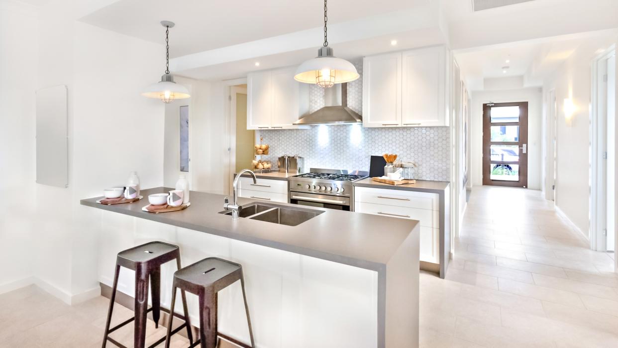 Modern kitchen interior at day time with a way to go to an outside door on the tile floor, there are plastic chairs near the counter.