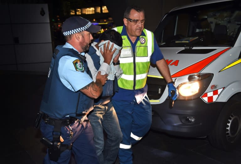 A policeman (L) and a paramedic (R) escort a hostage away from the scene during a hostage siege at a cafe in Sydney on December 16, 2014