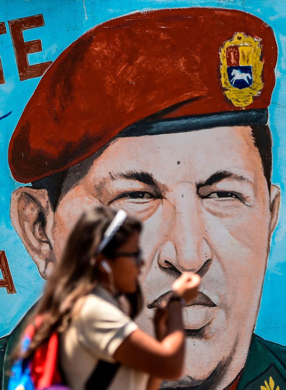 A student walks past a painting of late Venezuelan President Hugo Chavez on a wall in Caracas on January 29, 2019. - Venezuelan President Nicolas Maduro moved Tuesday to try to check the growing clout of opposition rival Juan Guaido as the United States tightened its stranglehold on the leftist regime's main source of revenues.