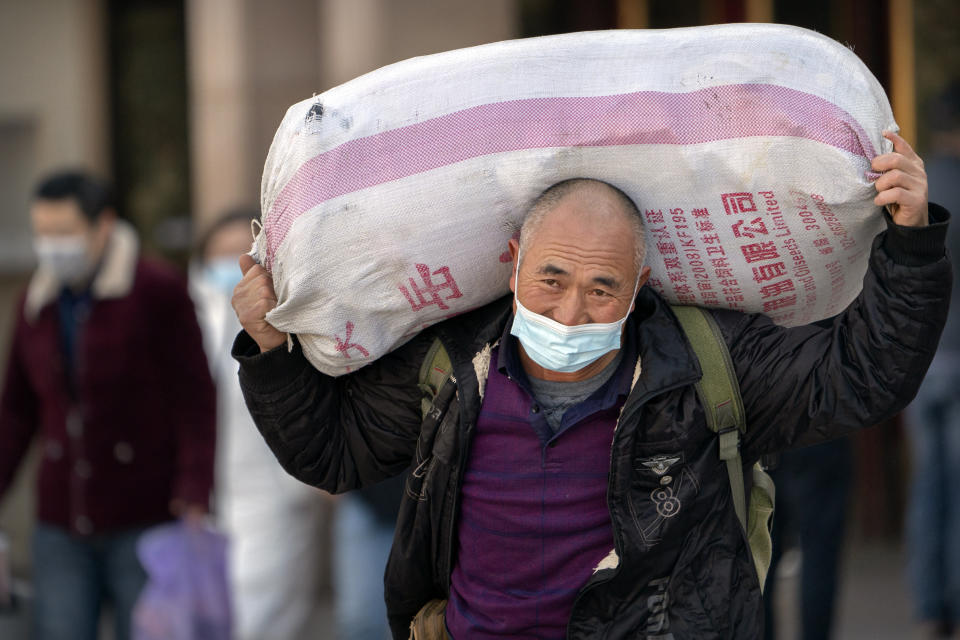A traveler wearing a face mask to protect against the spread of the coronavirus carries his luggage as he walks out of an exit at the Beijing Railway Station in Beijing, Thursday, Jan. 28, 2021. Efforts to dissuade Chinese from traveling for Lunar New Year appeared to be working. Beijing's main train station was largely quiet on the first day of the travel rush and estimates of passenger totals were smaller than in past years. (AP Photo/Mark Schiefelbein)
