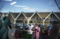 Adriana Perez, right, and her son, Sami, 12, are reflected in the glass window of Asthenis Pharmacy as they wait outside for a COVID-19 test in Providence, R.I., Tuesday, Dec. 7, 2021. Even as the U.S. reaches a COVID-19 milestone of roughly 200 million fully-vaccinated people, infections and hospitalizations are spiking, including in highly-vaccinated pockets of the country like New England. (AP Photo/David Goldman)