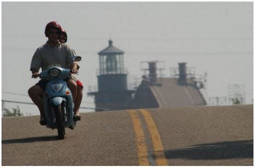 Two people ride a motorized scooter on Block Island.