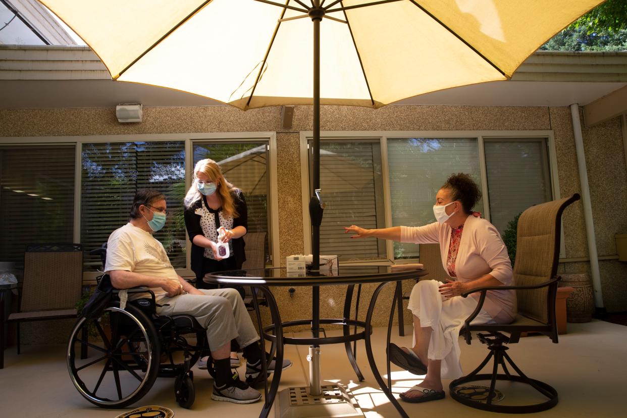 Deborah Trigueiro (R) visits her husband Douglas Smith, while Sarah Tongson, Director of Social Services, gives him some hand sanitizer, at the Life Care Center of Kirkland on Aug. 24, 2020 in Kirkland, Washington. This is only the second time they have seen each other in person since February when the coronavirus spread through the facility.