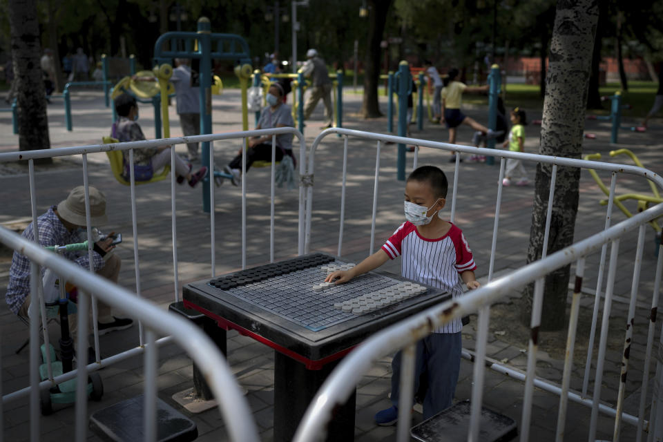 A child wearing a face mask plays alone on the barricaded black and white chess table to prevent residents gathering at a public park in Beijing, Tuesday, Aug. 30, 2022. (AP Photo/Andy Wong)