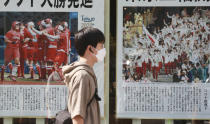 A man wearing face masks to protect against the spread of the coronavirus walks past extra papers reporting the start of the Tokyo Olympics in Tokyo Saturday, July 24, 2021. (AP Photo/Koji Sasahara)