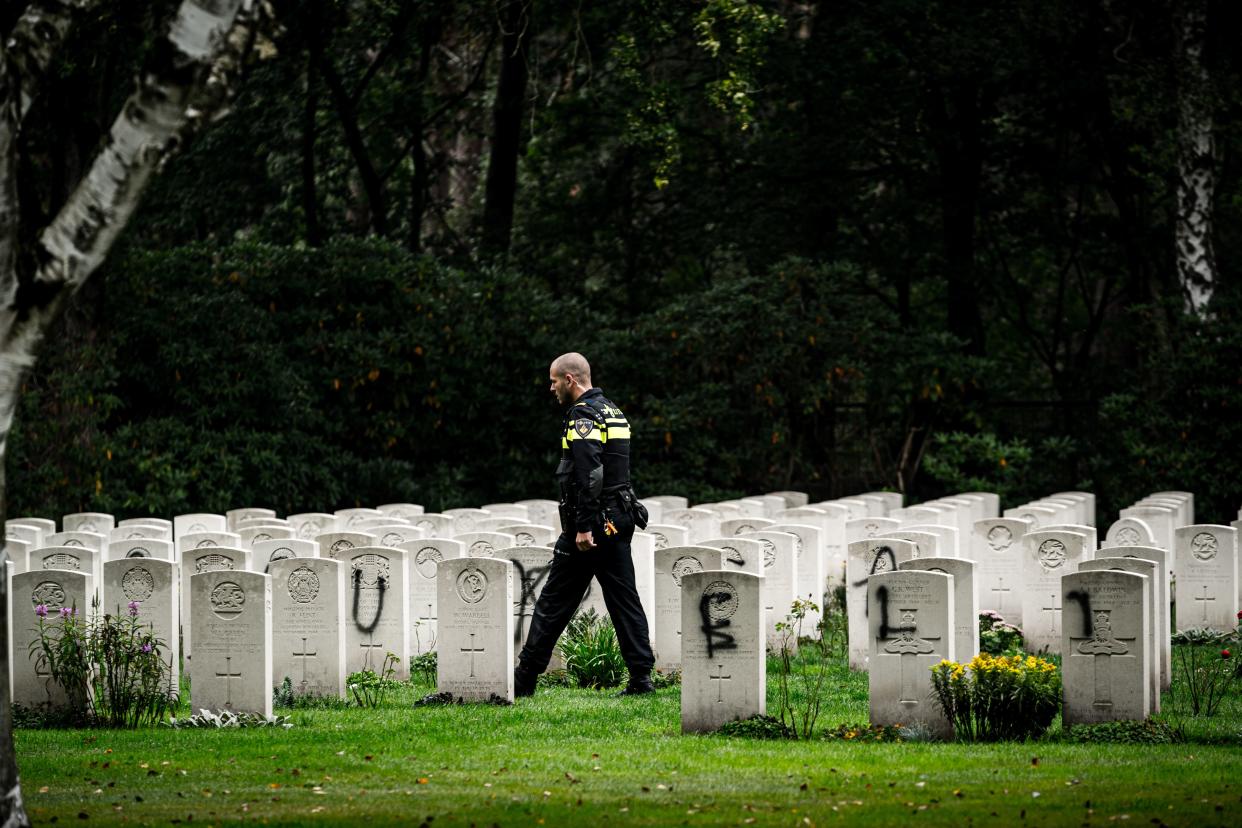 A police officer walks past graves which have been vandalised with graffiti, and a large swastika was daubed on the inner wall of the chapel in the British World War II Commonwealth Graves cemetery in Mierlo, east of Eindhoven, Netherlands, on September 13, 2019. (Photo by Rob Engelaar / ANP / AFP) / Netherlands OUT        (Photo credit should read ROB ENGELAAR/AFP/Getty Images)