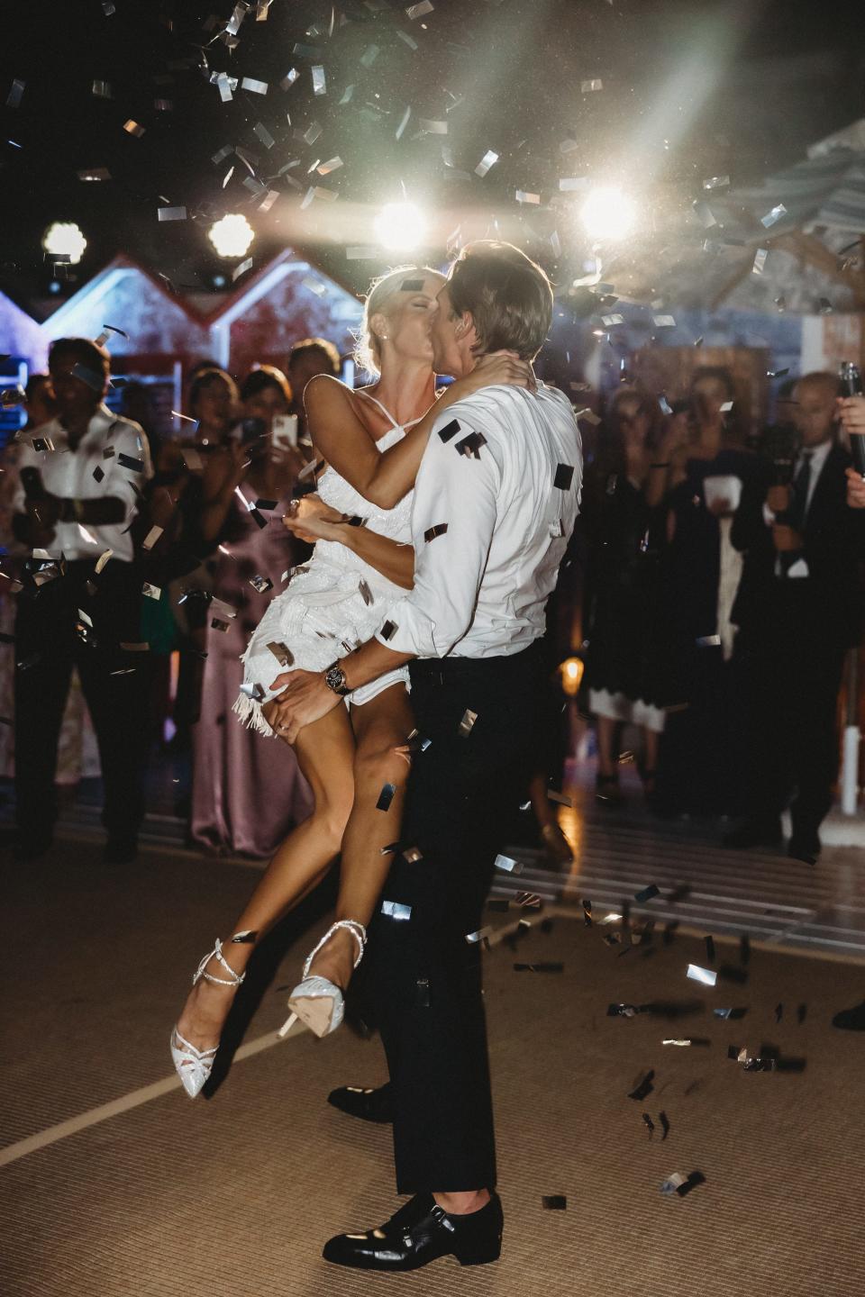 A groom lifts his bride as they dance and confetti falls around them.