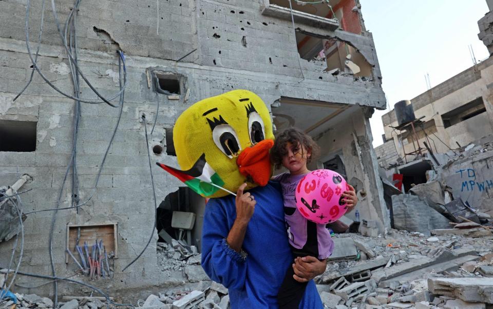 A Palestinian clown carries a child during a show amid the rubble of a building destroyed in the latest round of fighting between Israel and Palestinian militants, in Rafah in the southern Gaza Strip - SAID KHATIB/AFP