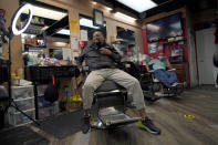 Mike Brown, a barber and health advocate, reacts while talking with colleagues and customers, Friday, April 9, 2021, in Hyattsville, Md. Brown is a member of the Health Advocates In Reach & Research (HAIR) program, which helps barbers and hair stylists to get certified to talk to community members about health. During the COVID-19 pandemic, Brown and a team of certified barbers have been providing factual information to customers about vaccines, a topic that historically has not been trusted by members of black communities because of the health abuse the race has endured over the years. (AP Photo/Julio Cortez)