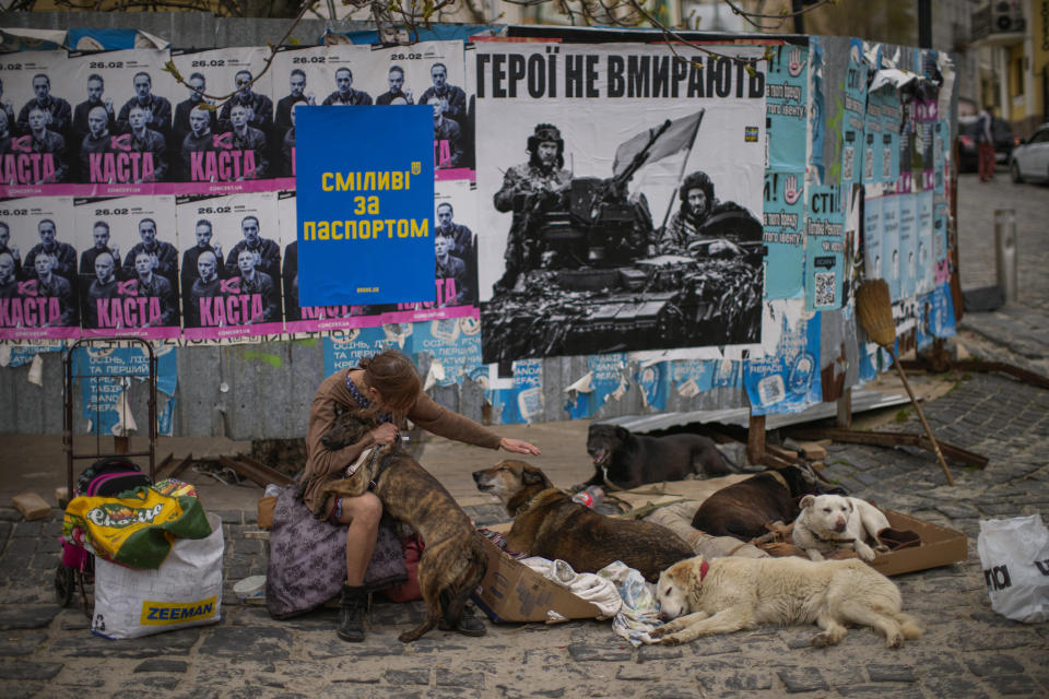 Ukrainian Iryna caresses dogs as she asks for money to support a centre for abandoned dogs next to a poster that reads in Ukrainian: "Heroes don't die", in Kyiv, Ukraine, Monday, April 25, 2022. Iryna is a volunteer who helps in a shelter where dozen of abandoned dogs have been moved in. (AP Photo/Francisco Seco)