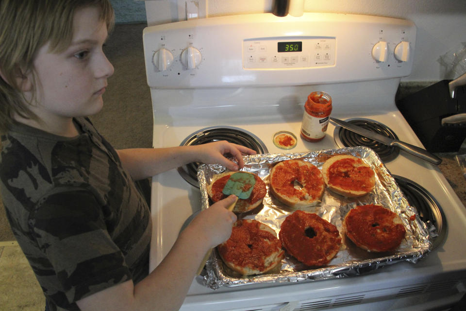 Jayden Messick, 9, helps his parents, Brian and Airis Messick, prepare lunch at their apartment in Anchorage, Alaska, on Wednesday, Nov. 11, 2020. The Messicks have had to turn to food banks after both lost their jobs in the economic downturn caused by the coronavirus pandemic. Airris, who just turned 30, found work in August, ironically, at the state unemployment office. “I hear people’s stories all day,” she says. “I listen to moms cry about not having money to take care of their kids. My heart aches for the people who get denied.” (AP Photo/Mark Thiessen)