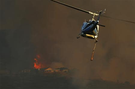 A fire fighting helicopter flies over a burning home on a hillside near San Marcos, California May 14, 2014. REUTERS/Mike Blake