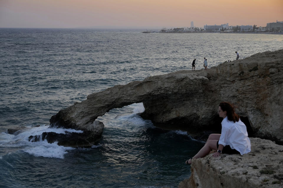 A woman sit on a rock as other people walk on the natural 'Love' bridge during sunset, at the Ayia Napa resort, in the eastern Mediterranean island of Cyprus, on Sunday, June 4, 2023. When the U.S. and U.K. in April included a handful of Cypriot nationals and Cyprus-registered companies as part of another global crackdown on 'enablers' helping Russian oligarchs skirt sanctions, the perception that the island nation somehow remains Moscow's financial lackey again loomed large. (AP Photo/Petros Karadjias)