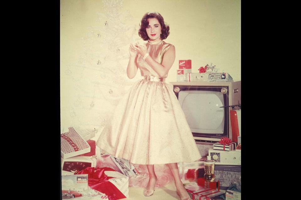 <p>Elizabeth Taylor looks festive in a gold satin A-line dress and a red lip, as she models for a holiday advert in 1950. </p>