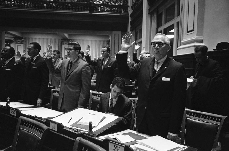 Rep.-elect Julian Bond, seated, fumbles through his desk in Atlanta, on Jan. 10, 1966, after he was refused his seat in the Georgia House of Representatives  Around him other Representatives raise their hands for the oath of office as they are sworn in. Bond, 25, became the center of a controversy when he endorsed a statement by the Student Nonviolent Coordinating Committee which charged the United States as being guilty of murder in Vietnam,