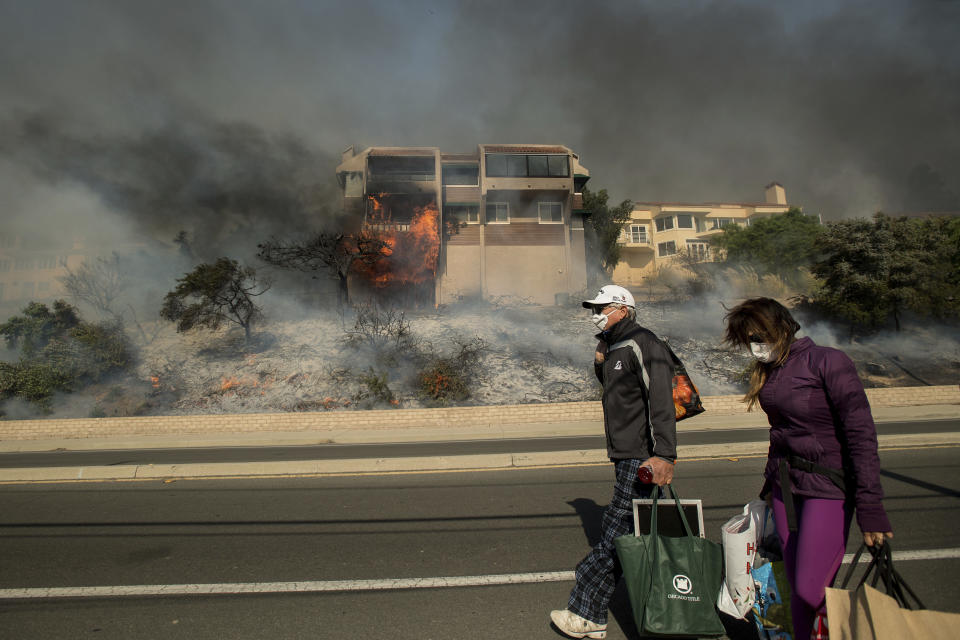 <p>James and Josie Ralstin carry belongings from their Ventura, Calif., home as flames from a wildfire consume another residence on Tuesday, Dec. 5, 2017. (Photo: Noah Berger/AP) </p>