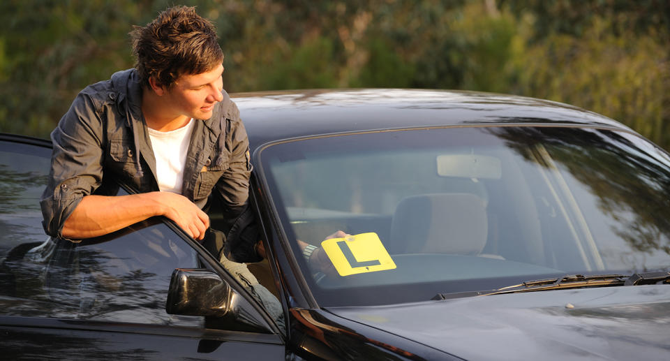 Young man putting his L plates onto the car window.