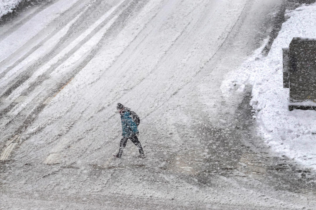 A pedestrian navigates a snow-covered street 