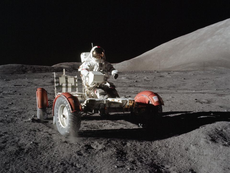 astronaut in spacesuit sits on lunar rover vehicle platform with wheels on the moon