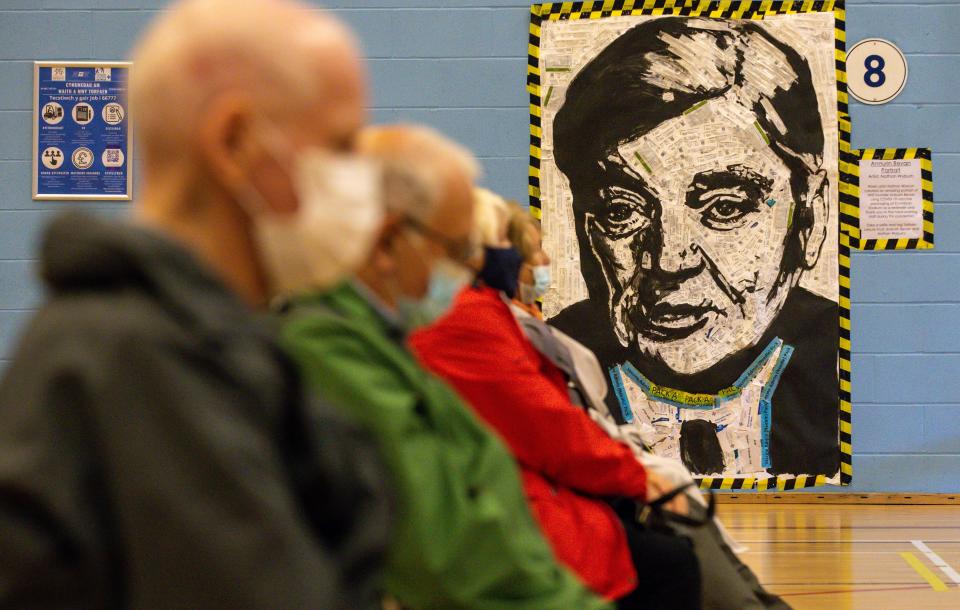 <p>CWMBRAN, WALES - OCTOBER 05:  Patients sit in front of a portrait of Aneurin Bevan the architect of the NHS  after receiving their boost vaccines on October 05, 2021 in Cwmbran, Wales. The Portrait is made up of used syringe packages by Welsh Artist Nathan Wyburn Patients who attend the vaccine centre are also being offered the option of a flu vaccine. The Welsh Government has also announced that all 12 to 15-year-olds will be invited by letter to have the vaccine and the majority being administered at mass vaccination centres. In some areas, vaccination will be carried out at schools. (Photo by Huw Fairclough/Getty Images)</p>
