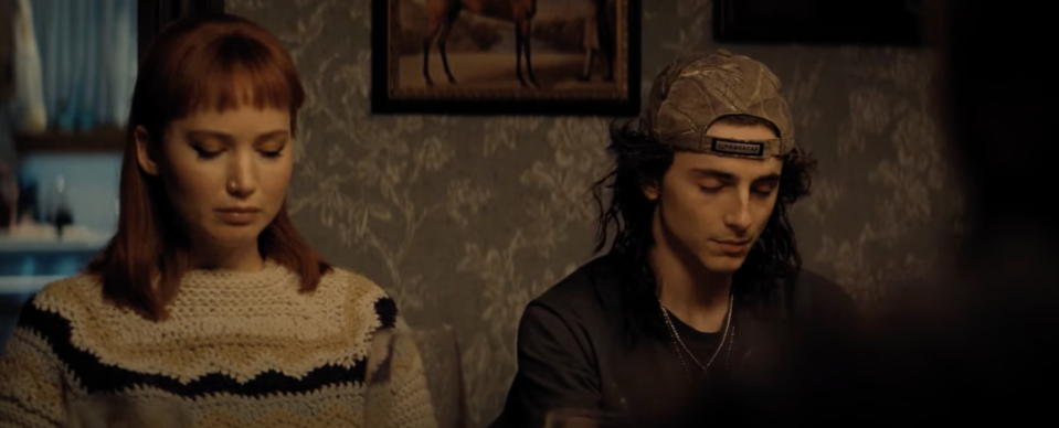 A young man and woman sit at a dinner table, praying