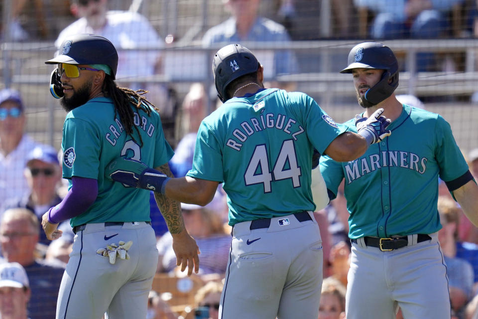 Seattle Mariners' Julio Rodriguez (44) and J.P. Crawford, left, celebrate after scoring against the Los Angeles Dodgers, with Mariners' Mitch Haniger, right, the next batter, during the fifth inning of a spring training baseball game Wednesday, March 13, 2024, in Phoenix. (AP Photo/Ross D. Franklin)