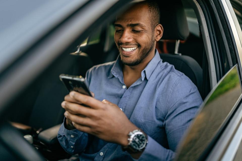 A person looks at their phone while sitting in the driver's seat of a car.