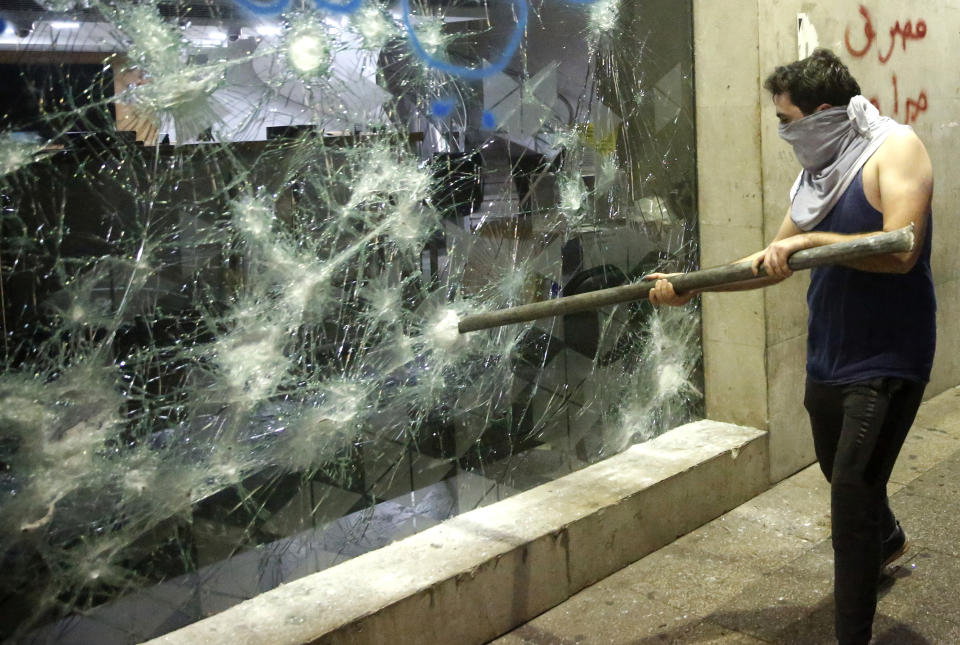 An anti-government protester smashes a bank widow, during ongoing protests against the Lebanese central bank's governor and against the deepening financial crisis, at Hamra trade street, in Beirut, Lebanon, Tuesday, Jan. 14, 2020. Lebanese security forces lobbed tear gas at protesters who responded with rocks outside the country's central bank Tuesday, a violent turn after demonstrators returned to the streets following a weekslong lull. (AP Photo/Hussein Malla)