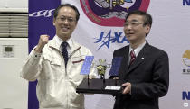 In this image made from video provided by JAXA, its project manager Yuichi Tsuda, left, and Hitoshi Kuninaka, Director General of ISAS/JAXA, pose with a Hayabusa2 model, during a press conference in Sagamihara, near Tokyo, Sunday, Dec. 6, 2020. Japanese space agency officials said Sunday they are excited about looking inside a capsule and analyzing soil samples of a distant asteroid asteroid subsurface that safely landed in the remote Australian Outback as planned. (JAXA via AP)