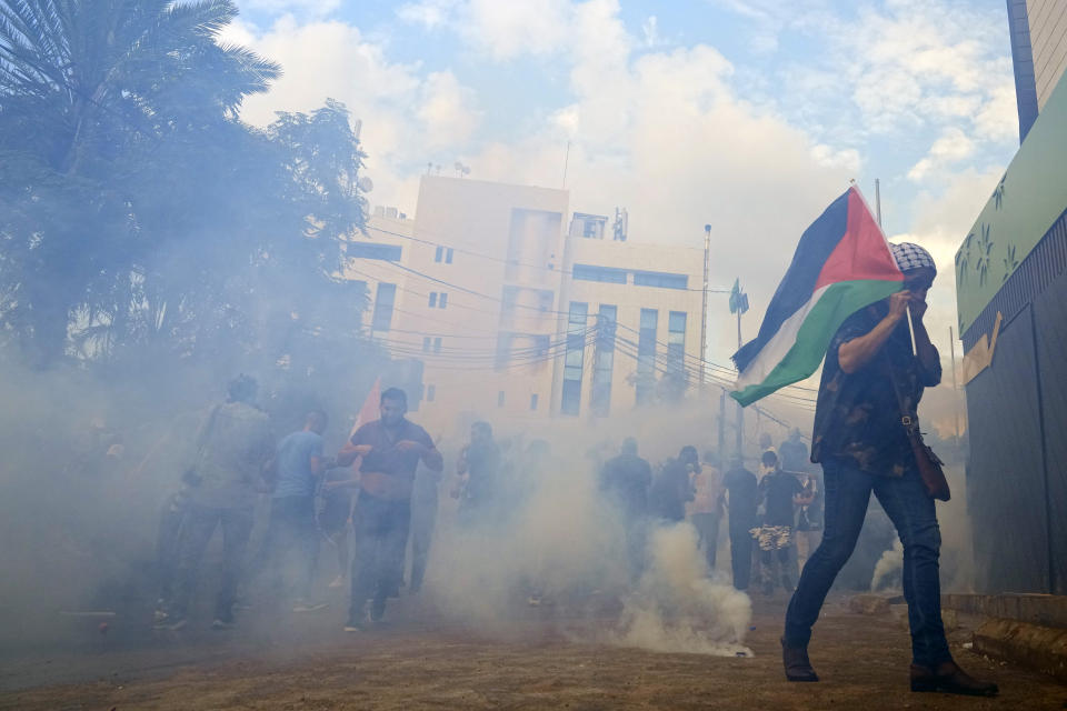 Protesters take cover from tear gas fired by riot police during a demonstration in solidarity with the Palestinian people in Gaza, near the U.S. embassy in Aukar, a northern suburb of Beirut, Lebanon, Wednesday, Oct. 18, 2023. Hundreds of angry protesters are clashing with Lebanese security forces in the Lebanese suburb Aukar near the United States Embassy. (AP Photo/Bilal Hussein)