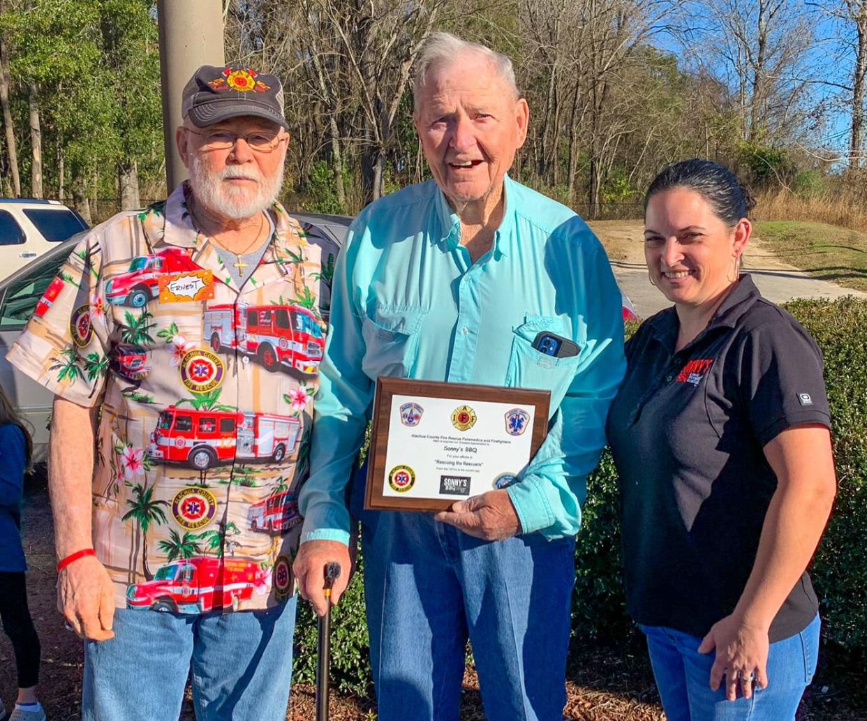 Sonny's BBQ founder Sonny Tillman, center, and Sonny's BBQ Alachua General Manager Cari Risgby, right, are honored Friday with the "Rescuers of Rescuers" award from Alachua County Fire Rescue's Ernest Wigglesworth, for more than 50 years of support of local first responders.