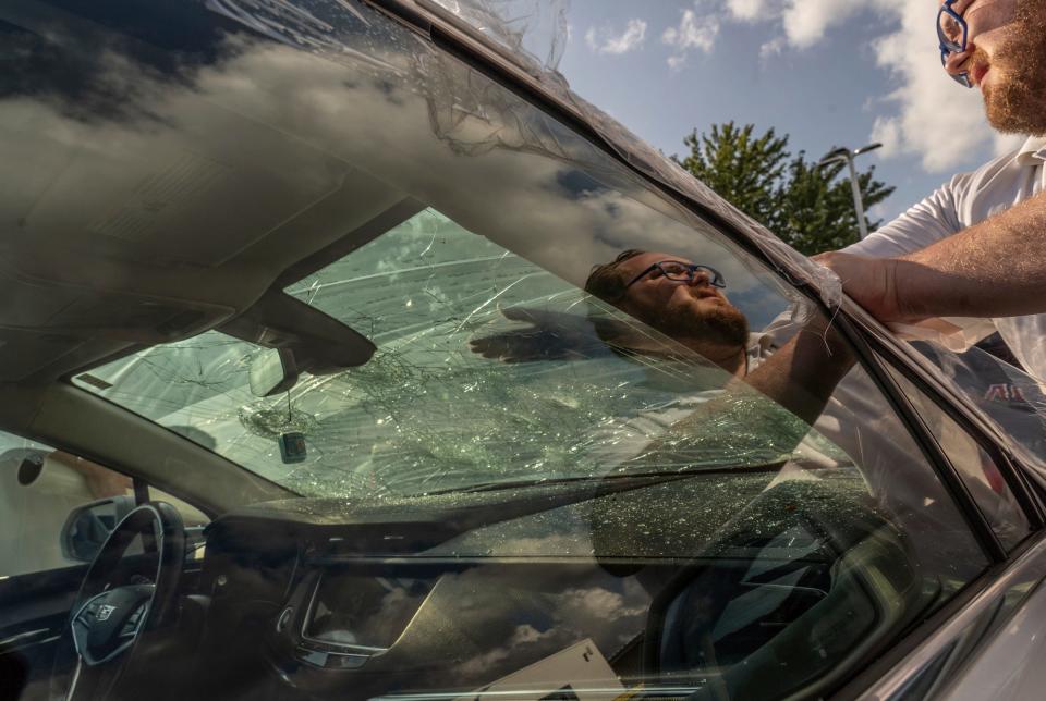 Todd Wenzel Buick GMC Of Davison employees work on covering glass from cars damaged by baseball-sized hail that came through Davison during a storm that moved through Michigan on Thursday, July 20, 2023.