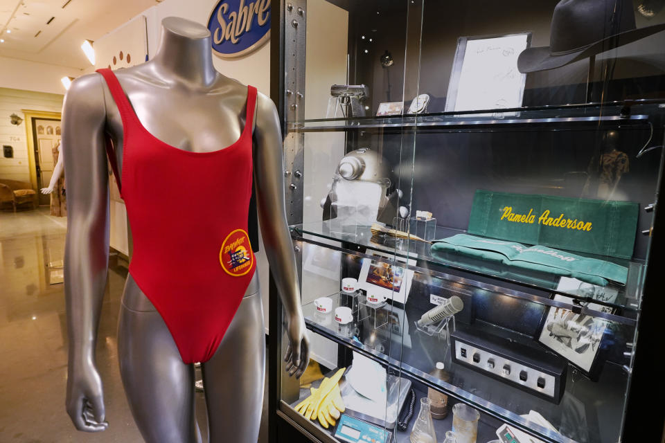 A red swimsuit used by actor Pamela Anderson on the television show "Baywatch" sits next to a display of other props from famous television shows, Thursday, April 27, 2023, in Irving, Texas. A dizzying number of props, sets, and costumes from television shows beloved by generations of viewers will be sold at auction next month. The collection James Comisar has spent over 30 years amassing includes "The Tonight Show" set Johnny Carson gave him after retiring, the timeworn living room from "All in the Family," and the bar where Sam Malone served customers on Cheers. (AP Photo/Tony Gutierrez)