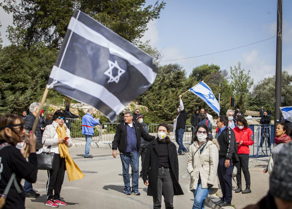 People wave Israeli flags during a protest outside the Israeli parliament in Jerusalem, Thursday, March 19, 2020. Hundreds of people defied restrictions on large gatherings to protest outside parliament Thursday, while scores of others were blocked by police from reaching the area as they accused Prime Minister Benjamin Netanyahu's government of exploiting the coronavirus crisis to solidify his power and undermine Israel's democratic foundations. (AP Photo/Eyal Warshavsky)