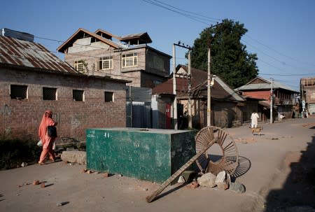 A Kashmiri woman walks past a blockade put up by residents to prevent Indian security force personnel from entering their neighborhood during restrictions, in Srinagar