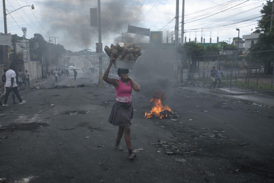 A street vendor walks past a barricade set up by demonstrators to protest against fuel price hikes and to demand that Haitian Prime Minister Ariel Henry step down, in Port-au-Prince, Haiti, Monday, Sept. 19, 2022. (AP Photo/Odelyn Joseph)