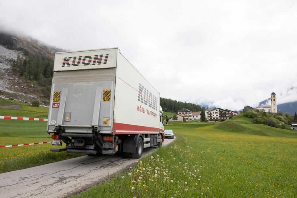 a truck that says "kuoni" is seen on a road with a closed area where rocks have fallen in Brienz-Brinzauls, Switzerland