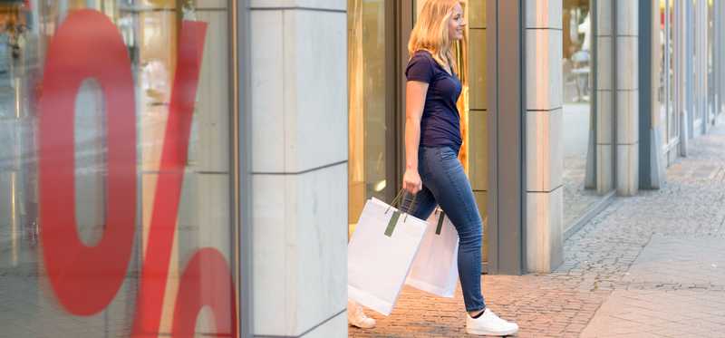 A woman walking out of a store with a shopping bag.