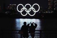 FILE - In this Dec. 1, 2020, file photo, a man and a woman look at the Olympic rings float in the water in the Odaiba section in Tokyo. Opposition to the Tokyo Olympics is growing with calls for a cancellation as virus cases rise in Japan. The International Olympic Committee and local organizers have already said another postponement is impossible, leaving cancellation, or going ahead, as the only options. (AP Photo/Eugene Hoshiko, File)