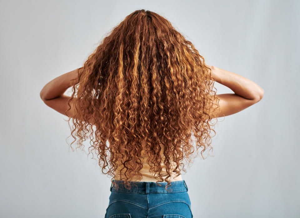 Person with long, curly hair shown from the back, wearing a light top and denim jeans