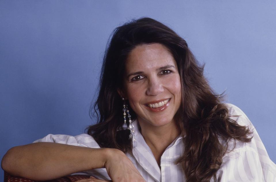 patti davis, wearing a white shirt, rests her right arm in front of her and smiles into the camera