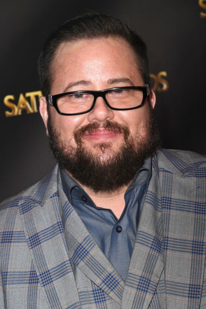 Man in plaid suit jacket smiling at a press event