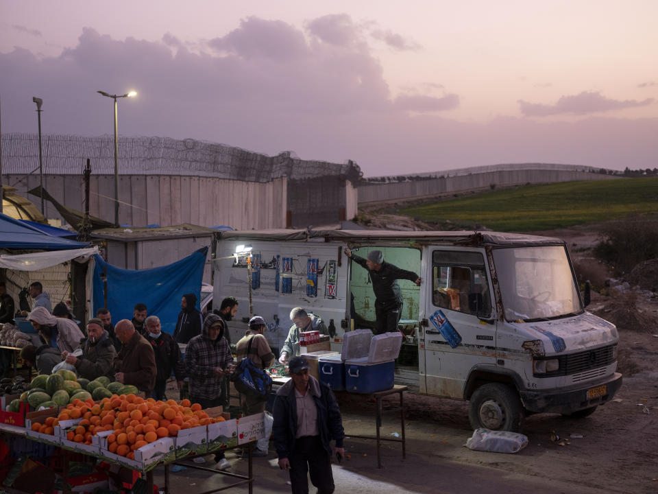 FILE - A vendor sells goods to Palestinian laborers as they cross from Israel back to the West Bank at the end of working day, next to a section of Israel's separation barrier in Meitar crossing in the West Bank, March 10, 2022. (AP Photo/Oded Balilty, File)