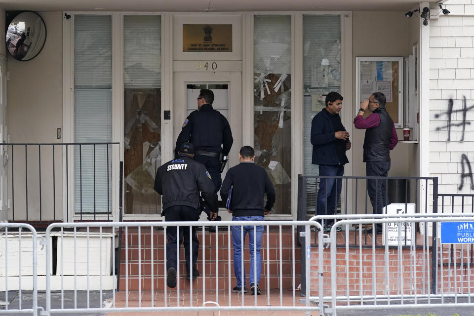 A San Francisco Police Officer, security guard and others stand in front of damage to the entrance to the Consulate General of India in San Francisco, Monday, March 20, 2023. San Francisco police had erected barriers and parked a vehicle nearby as people protested outside the Consulate General of India to protest the capture of Amritpal Singh. (AP Photo/Jeff Chiu)
