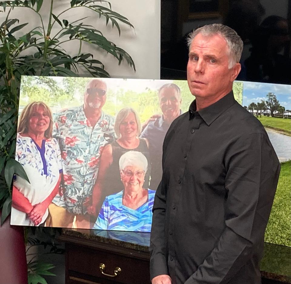 Bill Serge on Jan. 25, 2024, stands by a photo featuring his mother, Gloria Serge, in blue, who died after being pulled into the water in February 2023 by an alligator in St. Lucie County.
