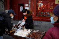 People wearing face masks buy food from a stall outside a restaurant after the novel coronavirus outbreak in Beijing