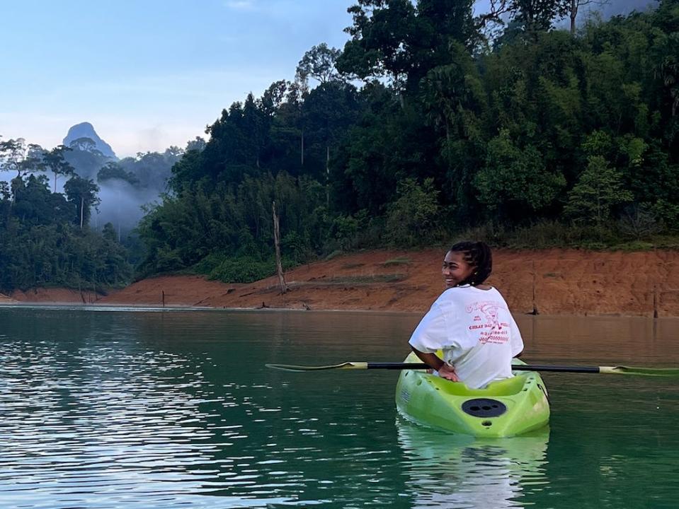 domonique kayaking in a lake in thailand with trees and mountains in the background