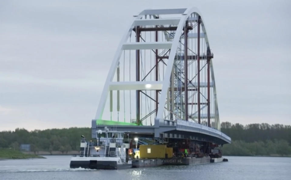 In this image taken from video released by Netherlands Department of Waterways and Public Works, showing a 200-metre (656-feet) long bridge taking a slow cruise through the heart of Rotterdam as it heads towards its new temporary home near the city's busy port area early Monday May 10, 2021 in Rotterdam. Tug boats moved the 20 metres (65 feet) wide and with a 40 metre (131 feet) high arch, Suurhoff Bridge early on Monday supported on pontoons under a series of other bridges on the Maas River that bisects the Dutch city. (RIJKSWATERSTAAT Department of Waterways and Public Works via AP)